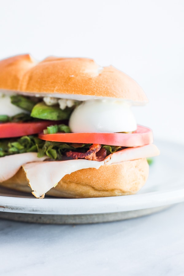 A sandwich layered with deli chicken, canon, lettuce, tomato, and hardboiled egg