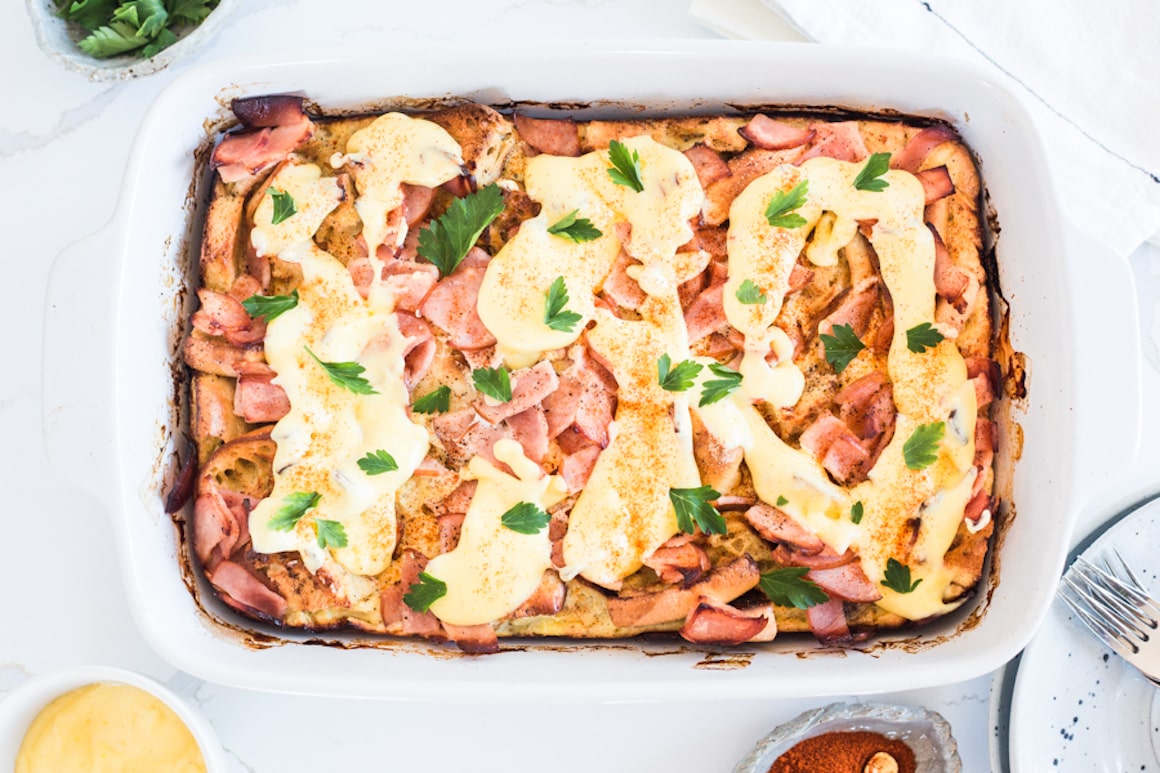 A baking dish filled with eggs Benedict casserole drizzled with hollandaise sauce and topped with parsley