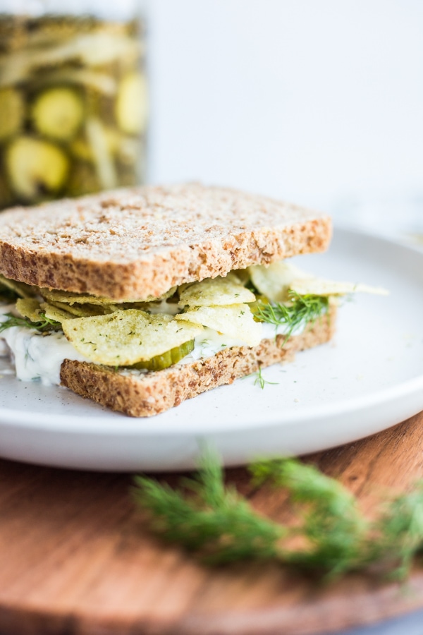 A sandwich with creamy sauce, pickles, and dill pickle potato chips