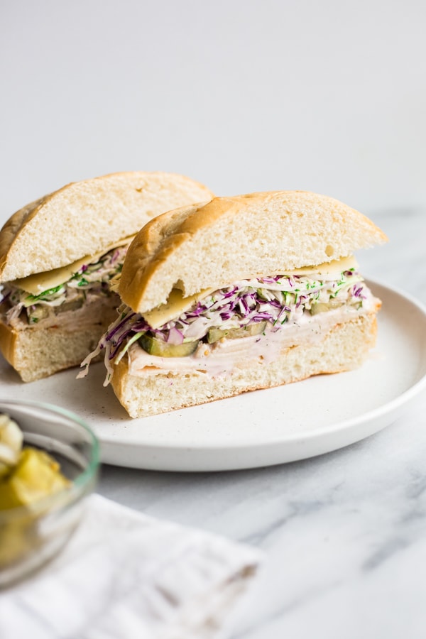 A sliced turkey sandwich with pickles and dill slaw