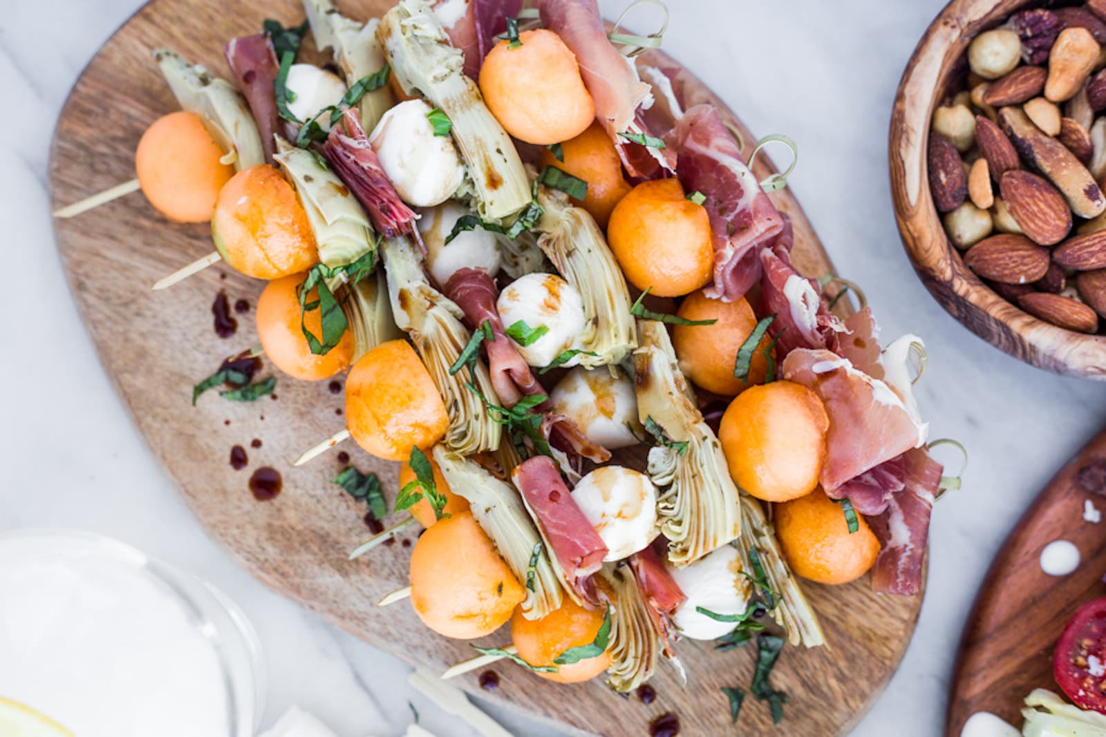 Skewers with melon, prosciutto, and marinated artichoke hearts on a wooden platter
