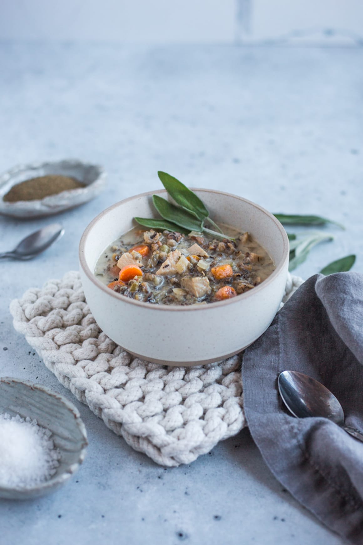A cream bowl filled with turkey and wild rice soup topped with sage leaves