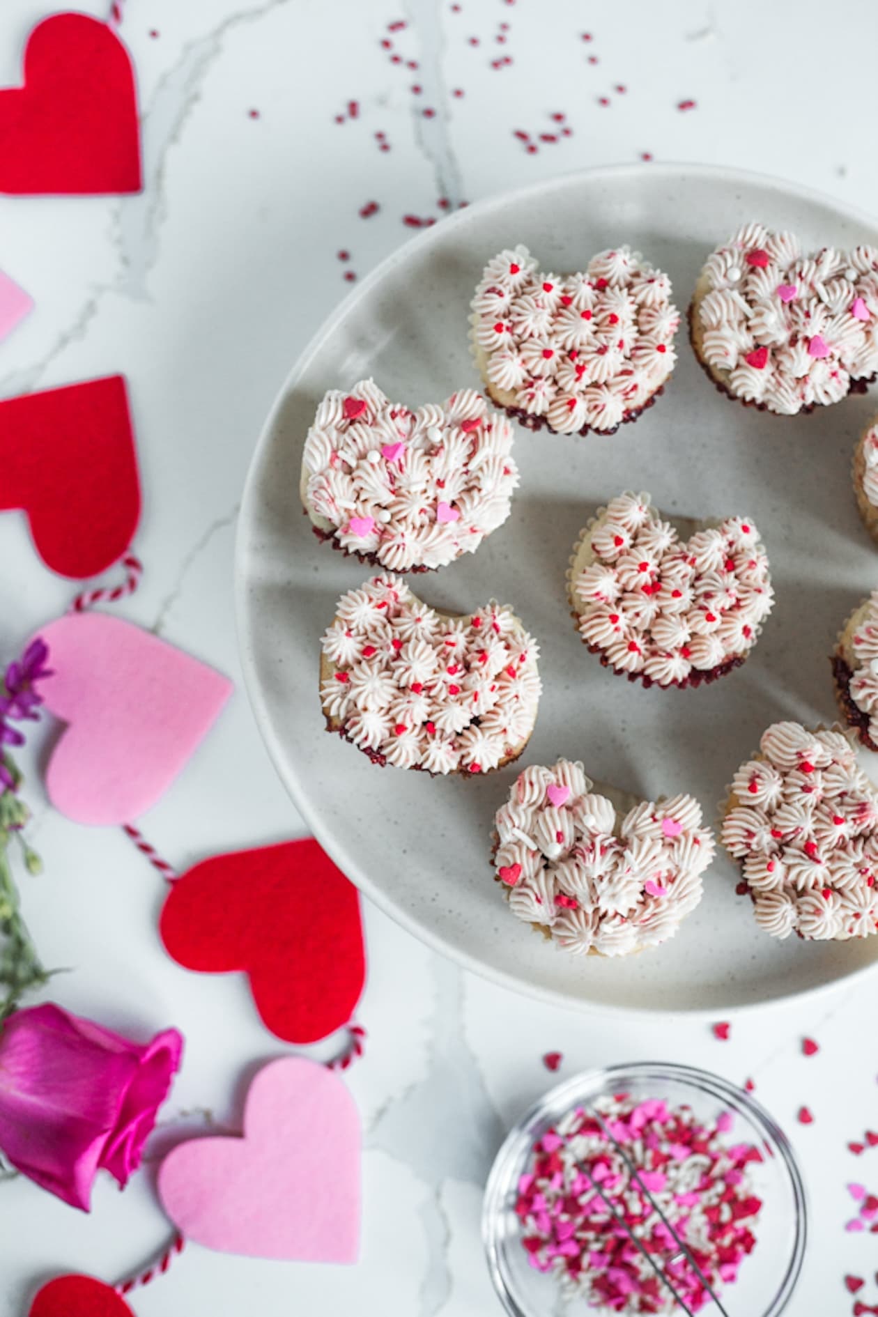 A plate of heart shaped cupcakes topped with red and pink sprinkles