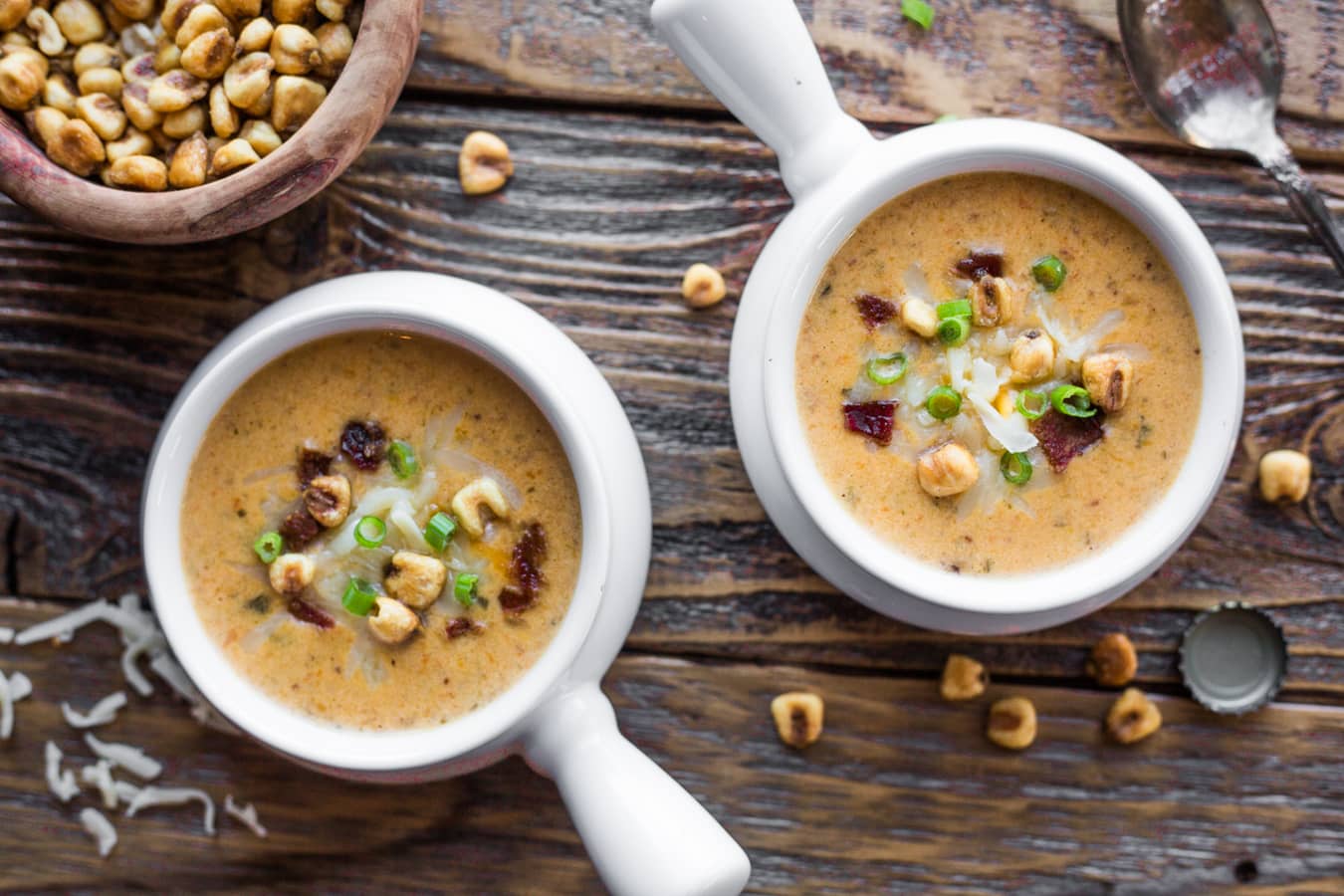Two soup bowls filled with beer cheese soup topped with bacon, green onions, and corn nuts