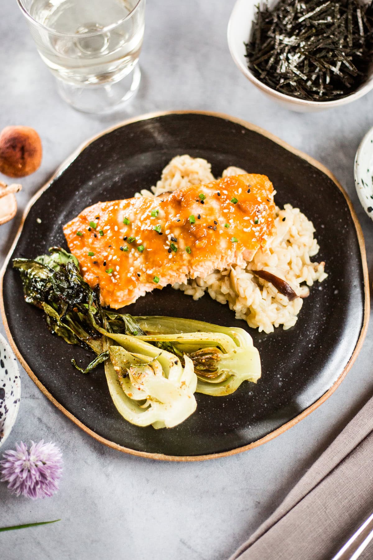 A black plate topped with miso glazed salmon, risotto, and bok choy