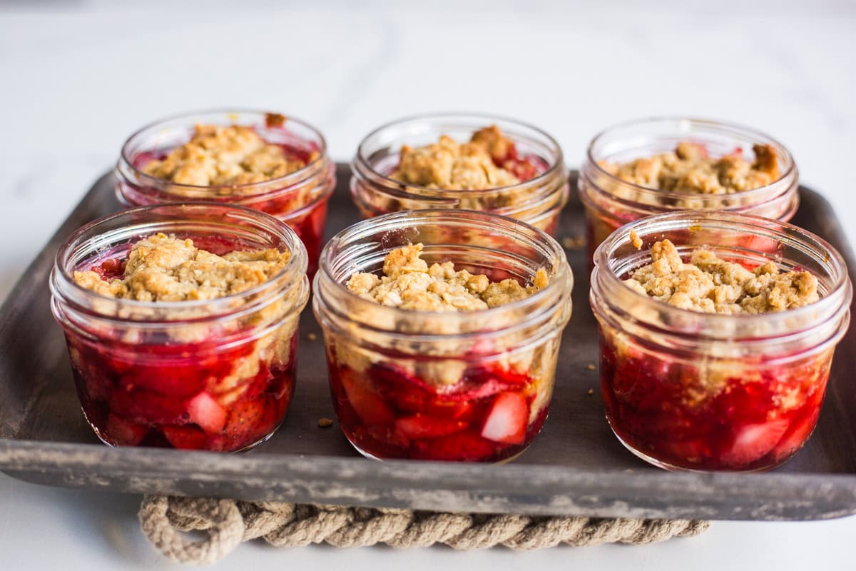 mason jars filled with baked strawberries and raspberries topped with an oatmeal crumble