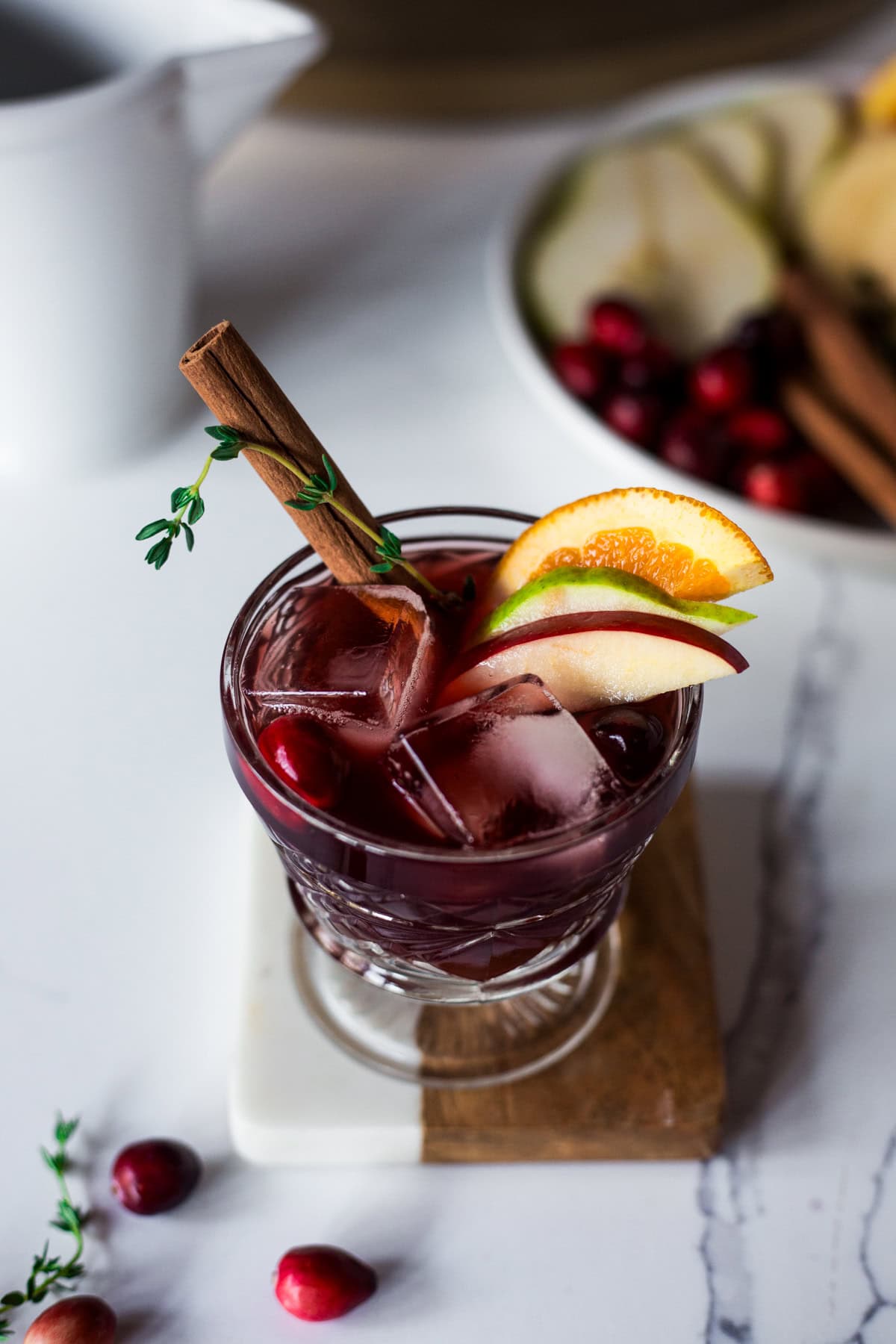 A glass of red wine sangria garnished with a cinnamon stick, apple, orange, and pear slice