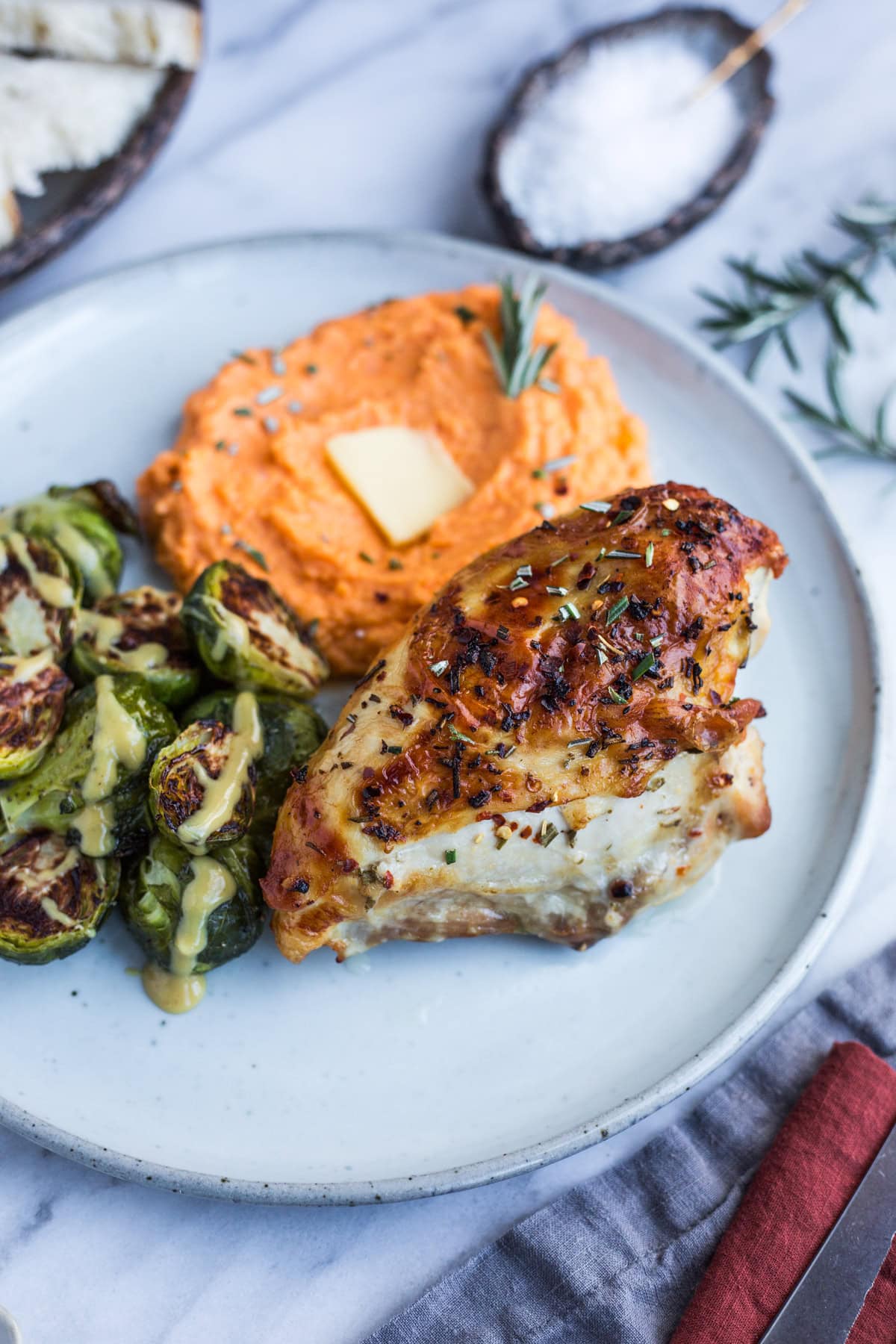 A plate topped with rosemary and garlic roasted chicken, whipped sweet potatoes, and Brussels sprouts drizzled with maple dijon glaze