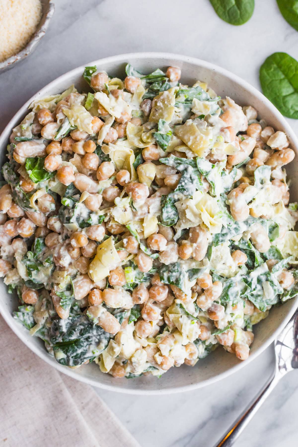 A bowl filled with a creamy dense bean salad with spinach and artichokes