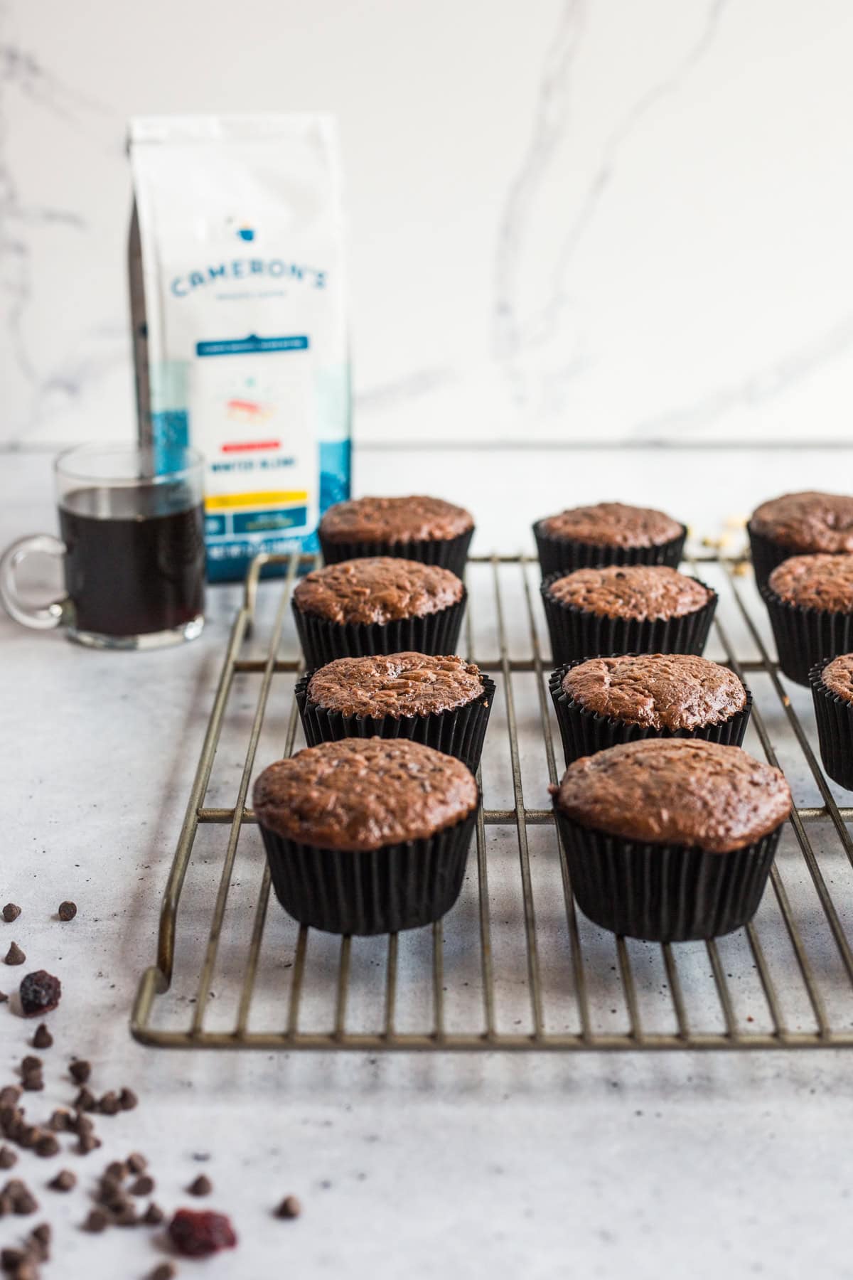 Chocolate muffins on a cooling rack with a cup of coffee in the background