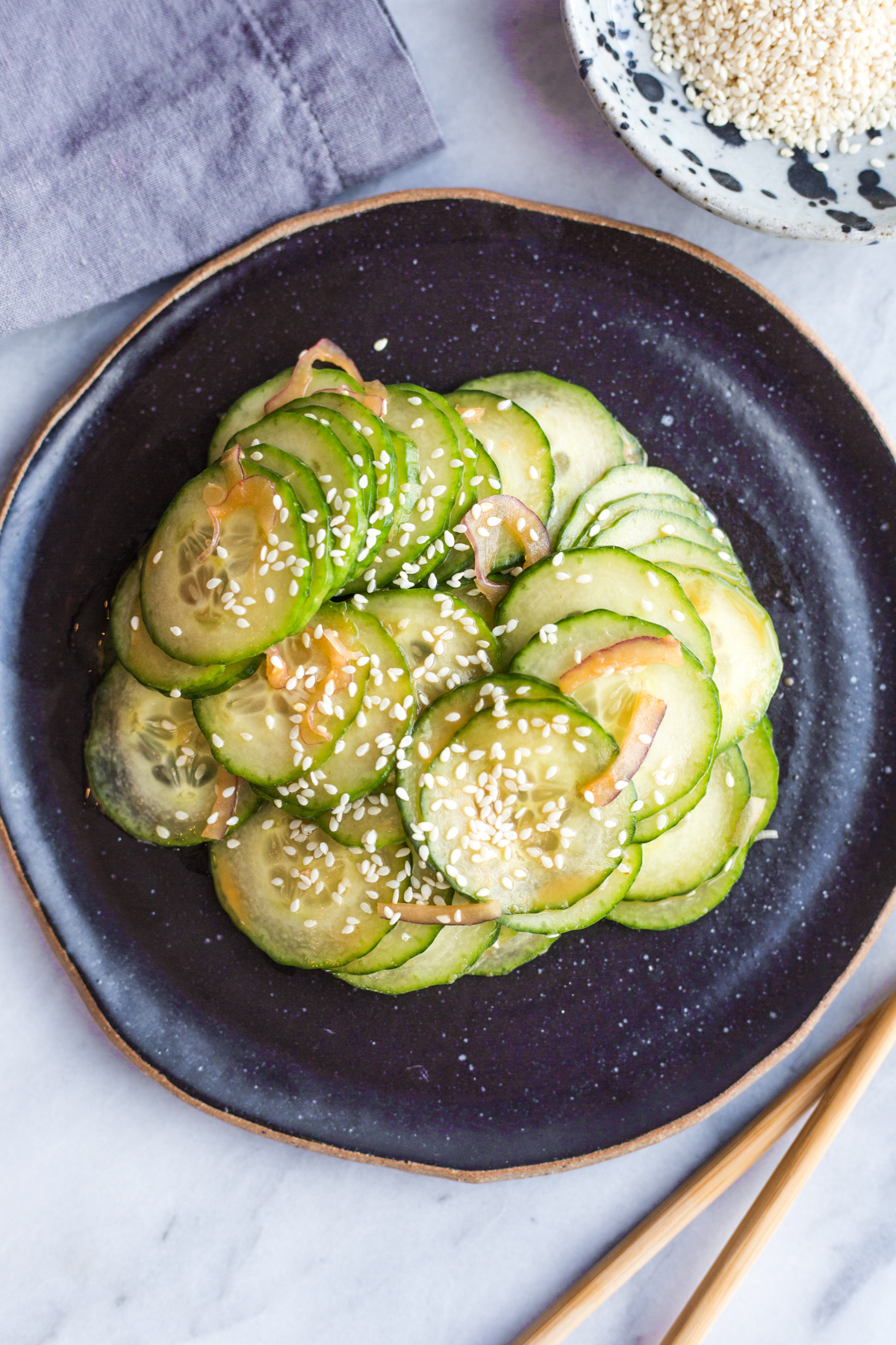 A black platter topped with a sliced cucumber salad