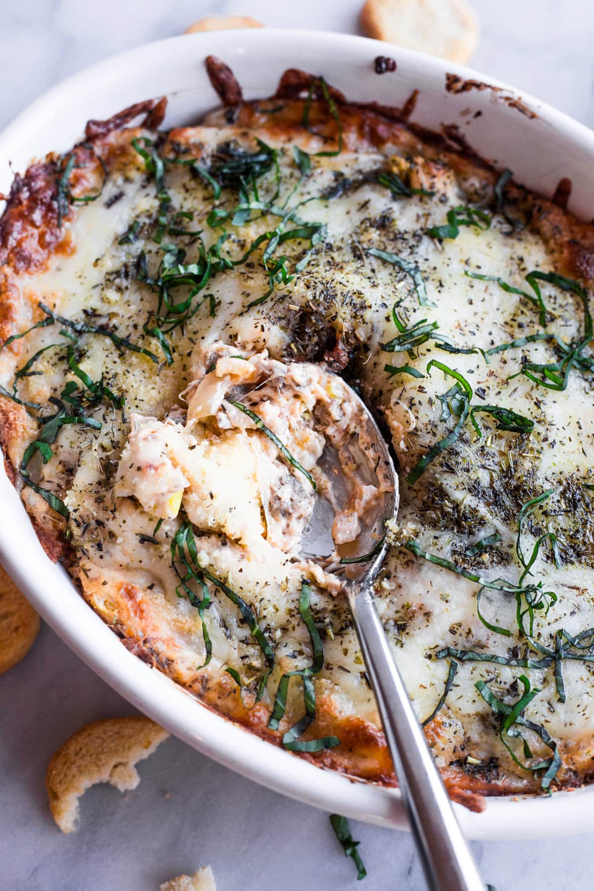 A spoon sitting in spicy Italian sausage dip in a white baking dish