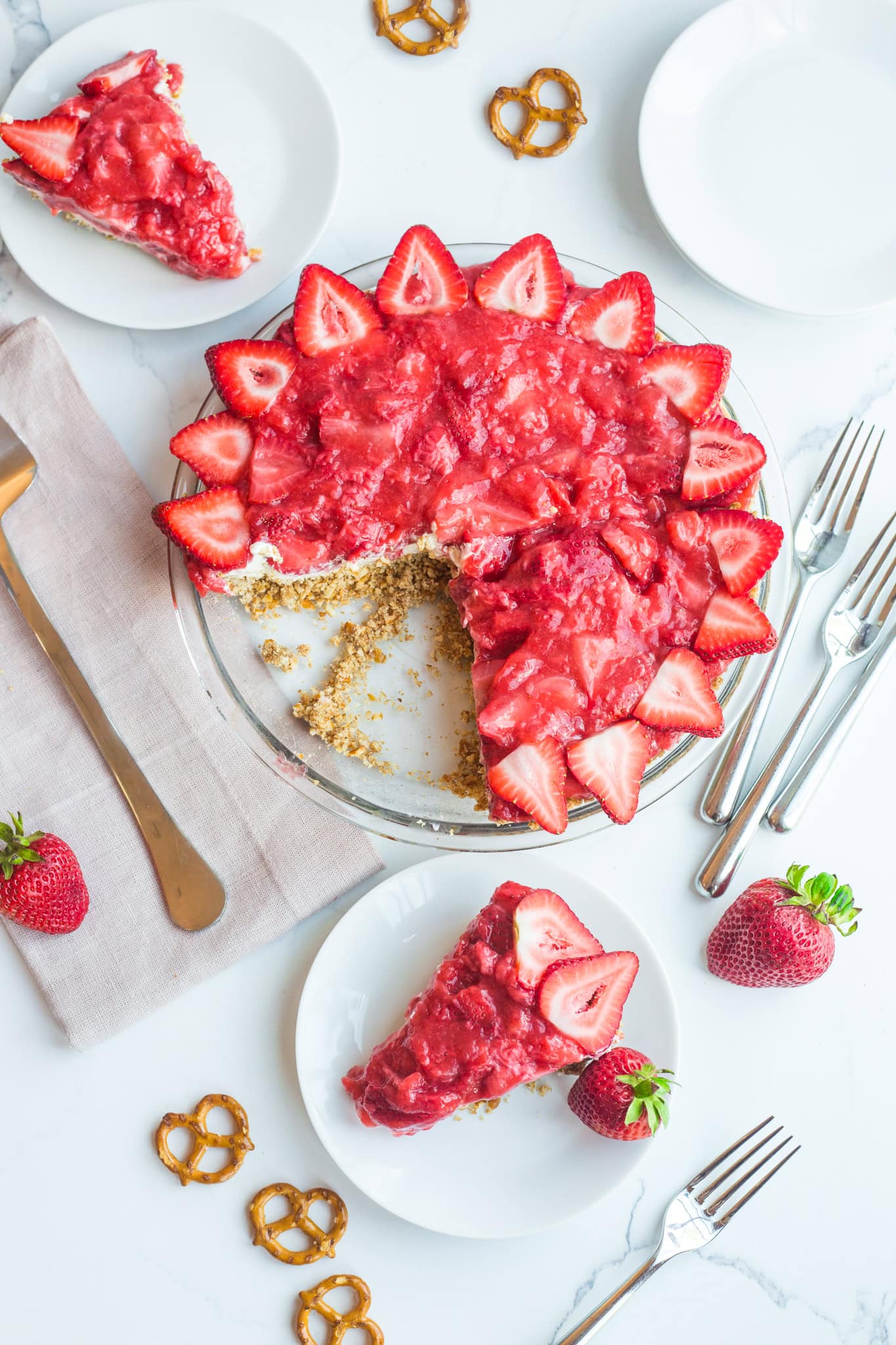 A strawberry pie surrounded with stacked plates, strawberries, and pretzels