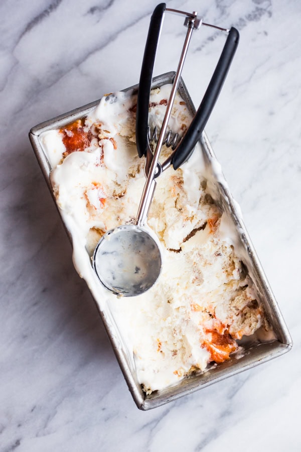 A loaf pan filled with peach cobbler ice cream topped with an ice cream scoop