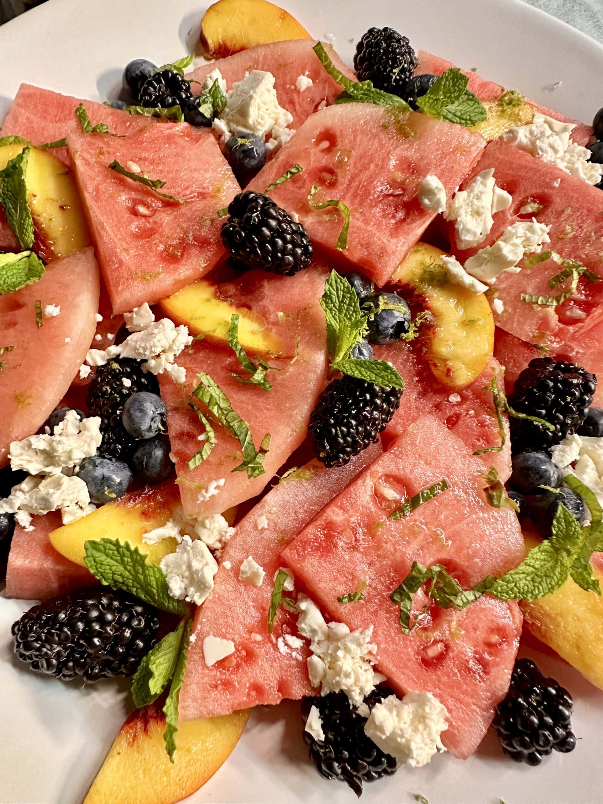 A watermelon, peach, and blackberry salad topped with mint and feta